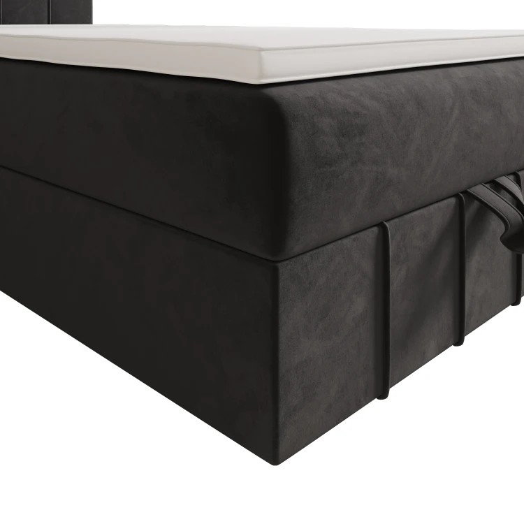 Nahaufnahme der Ecke eines dunklen Boxspringbettes mit Samtbezug und Matratzentopper.